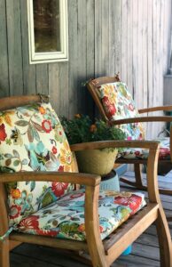 Two wooden armchairs with vibrant floral cushions on a cozy porch setting. Ideal for relaxing moments.